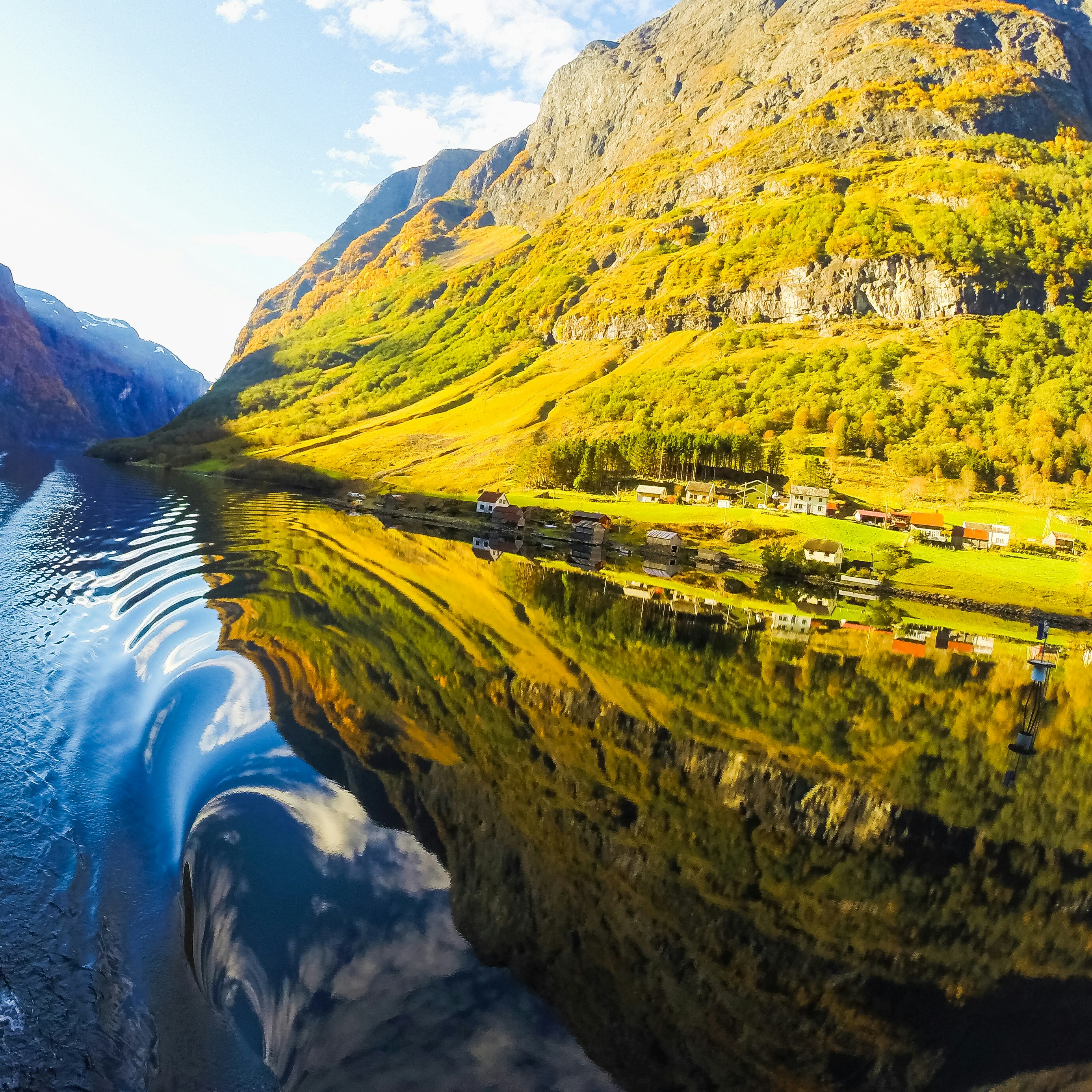 houses near mountain beside lake under blue and white skies